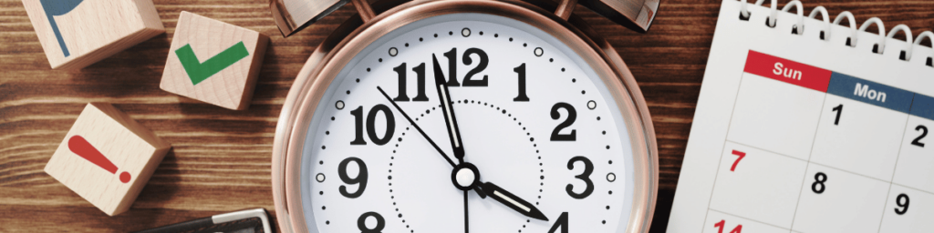Reloj de manecillas marcando las 3:57, fragmento de calendario y piezas de madera con signos. (Flexibilidad horaria cursos del SEPE)
